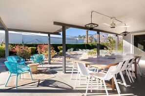 An outdoor patio with a table and chairs, a ceiling fan, and a view of a landscaped garden. - Salt & Sun Palm Springs by Navigate Stays (Palm Springs)