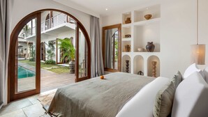 A bedroom with a large bed, a view of a pool and outdoor area, and a shelf with decorative items. - Villa Amara in Kuta with 7 bedrooms and 7 bathrooms (Kuta)