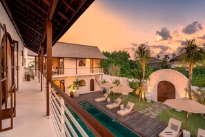 A poolside area with lounge chairs, a wooden deck, and a stone wall. - Villa Amara in Kuta with 7 bedrooms and 7 bathrooms (Kuta)