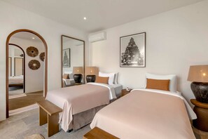 Hotellihuone, jossa on kaksi sänkyä, penkki, peili ja seinällä oleva kehystetty kuva.