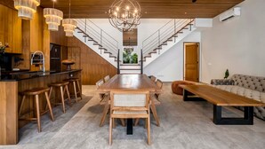 Eine moderne Küche mit einer Holzinsel, ein Essbereich mit großem Tisch und Stühlen sowie eine Treppe, die in ein Obergeschoss führt.