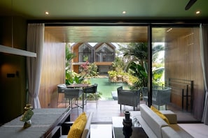 A modern interior with a dining area, a sofa, and a view of an outdoor garden and pool. - Sunset Lagoon Rice Field Villa (Ubud)