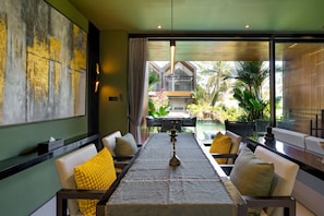 A dining area with a table, chairs, and a view of the outdoors. - Sunset Lagoon Rice Field Villa (Ubud)
