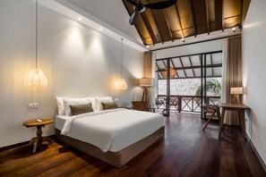 Ein modernes Hotelzimmer mit einem großen Bett, zwei Nachttischlampen, Holzboden, Deckenventilator und einem Balkon mit Sitzgelegenheit.