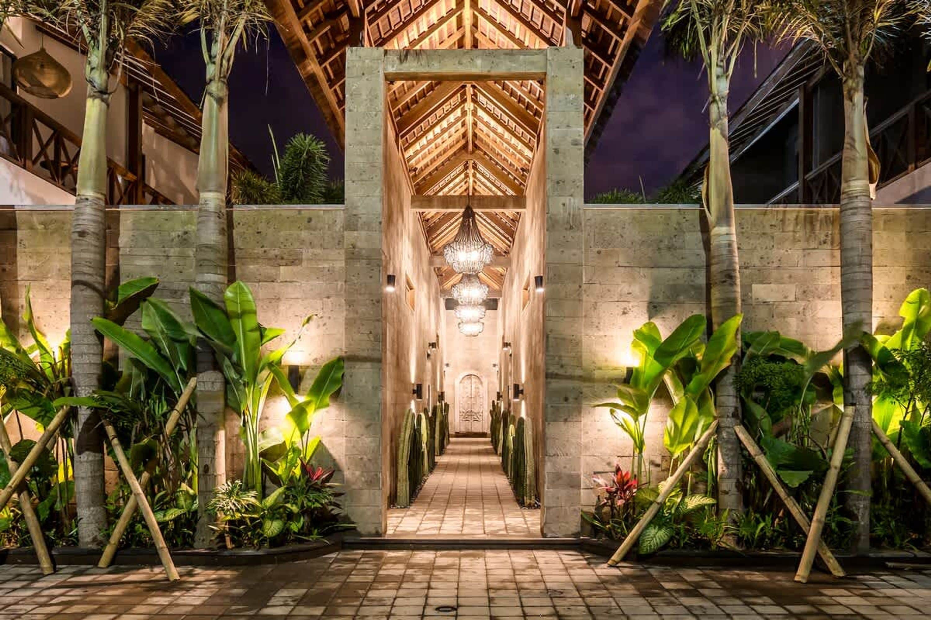 A well-lit pathway leading to a building with a wooden roof structure and a central chandelier.