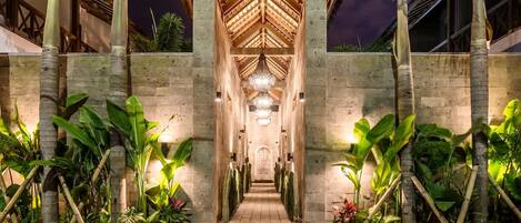 A well-lit pathway leading to a building with a wooden roof structure and a central chandelier.