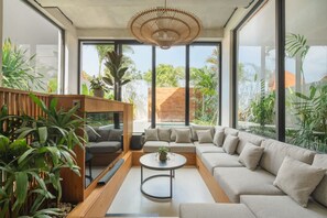 A modern living room with a sofa, a coffee table, and a TV. There are large windows and plants. - Makia Loft in Canggu (Canggu)