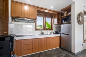 Une cuisine moderne avec des meubles en bois, un réfrigérateur en acier inoxydable et une fenêtre donnant sur un paysage verdoyant.
