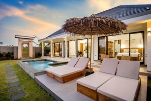Ein modernes Haus mit Swimmingpool, Liegestühlen und einem großen Sonnenschirm.