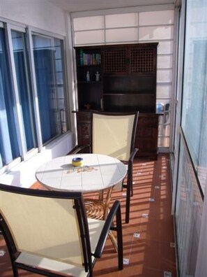 Ein Balkon mit rundem Tisch und Stühlen, einem Bücherregal und Blick durch das Fenster.