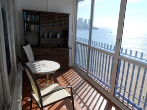 Ein Balkon mit Blick aufs Wasser, ein Stuhl, ein Tisch und ein Bücherregal.