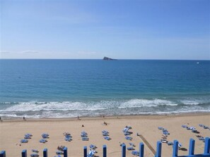A beach with rows of blue beach chairs and umbrellas, a sandy shore, and a distant island. - Palmeras 9D in Benidorm (Benidorm)