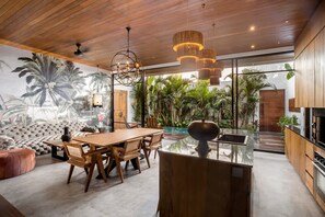 A modern kitchen with a large island, wooden cabinetry, and a view of a lush garden. - Nusantara Loft Ambon (Pererenan)
