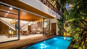 Ein modernes Haus mit Schwimmbad, Holzterrasse und tropischen Pflanzen.