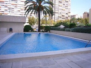 A swimming pool with a tiled edge, surrounded by a paved area and a tall residential building in the background. - Torre Levante 6B in Benidorm (Benidorm)