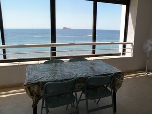 A table with a patterned tablecloth, two chairs, a window with a view of the sea, and a standing fan. - Torre Levante 6B in Benidorm (Benidorm)