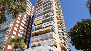 Un edificio alto con numerosi balconi, un ristorante con posti a sedere all'aperto e una palma.