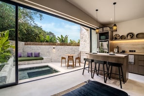 Eine moderne Küche mit Bar, ein Essbereich mit Blick auf einen Pool und einer Steinwand.