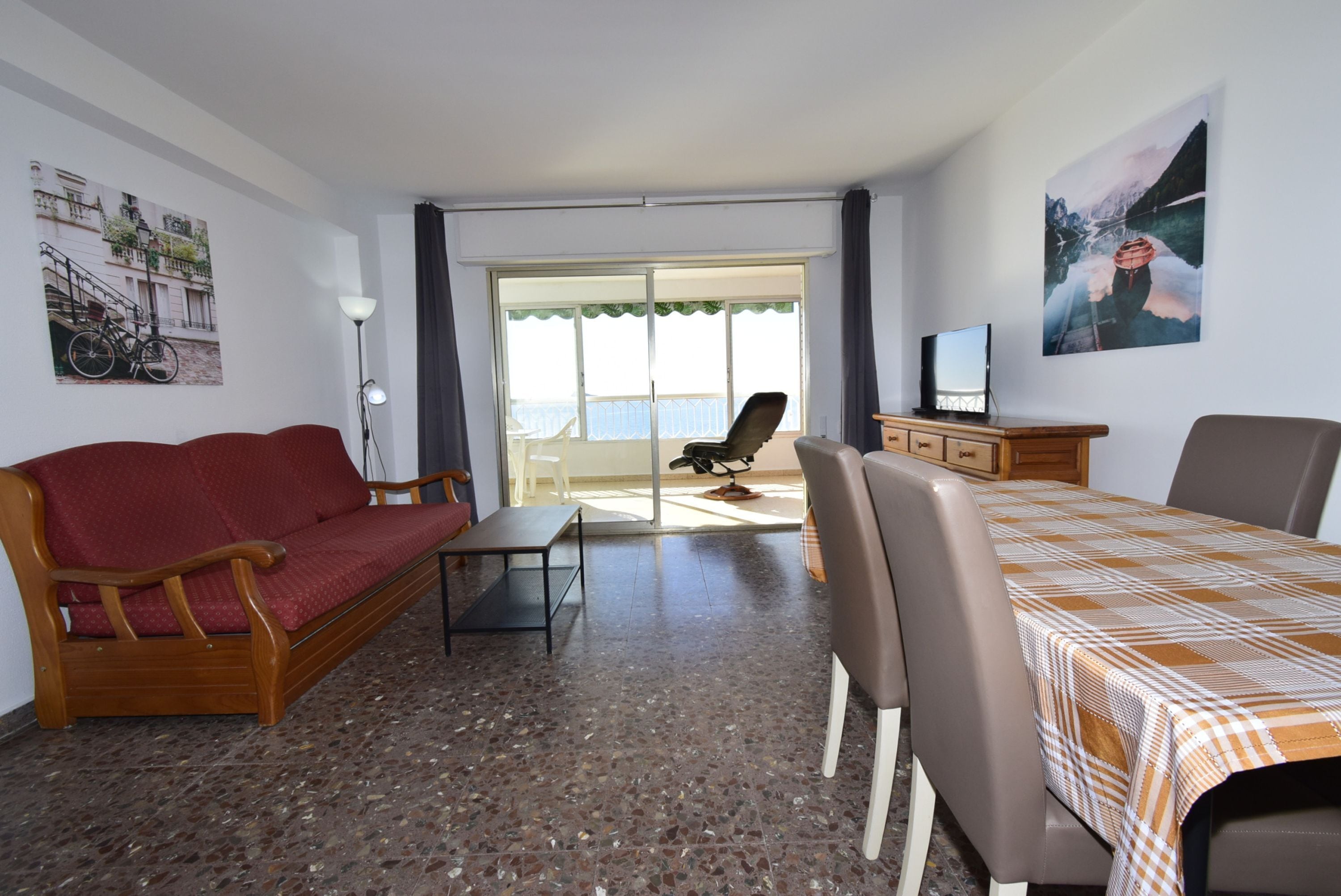 Una habitación con sofá, mesa, sillas, televisor y un balcón con vistas.