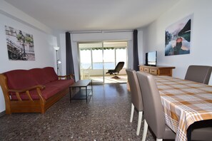 Una habitación con sofá, mesa, sillas, televisor y un balcón con vistas.