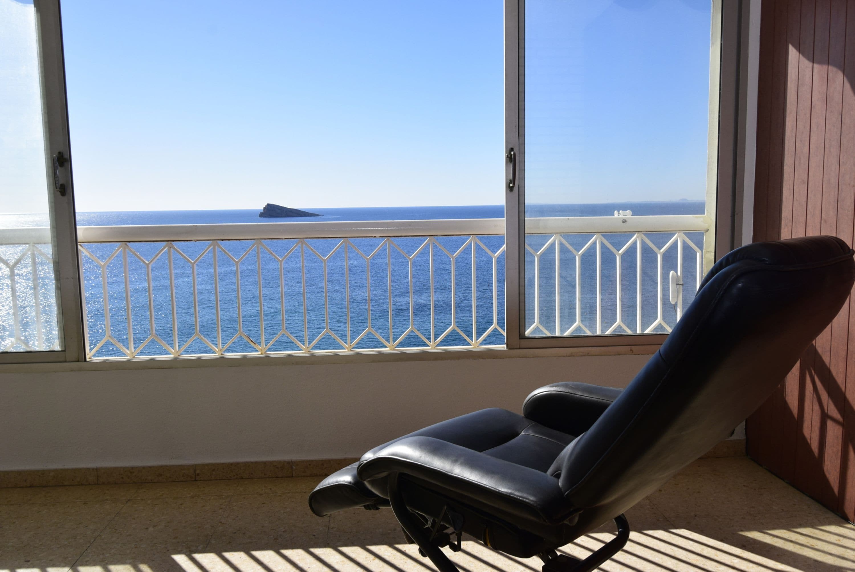 Un balcón con vista al mar, una silla negra y una barandilla blanca.