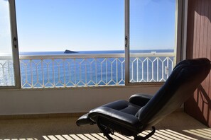 Un balcón con vista al mar, una silla negra y una barandilla blanca.