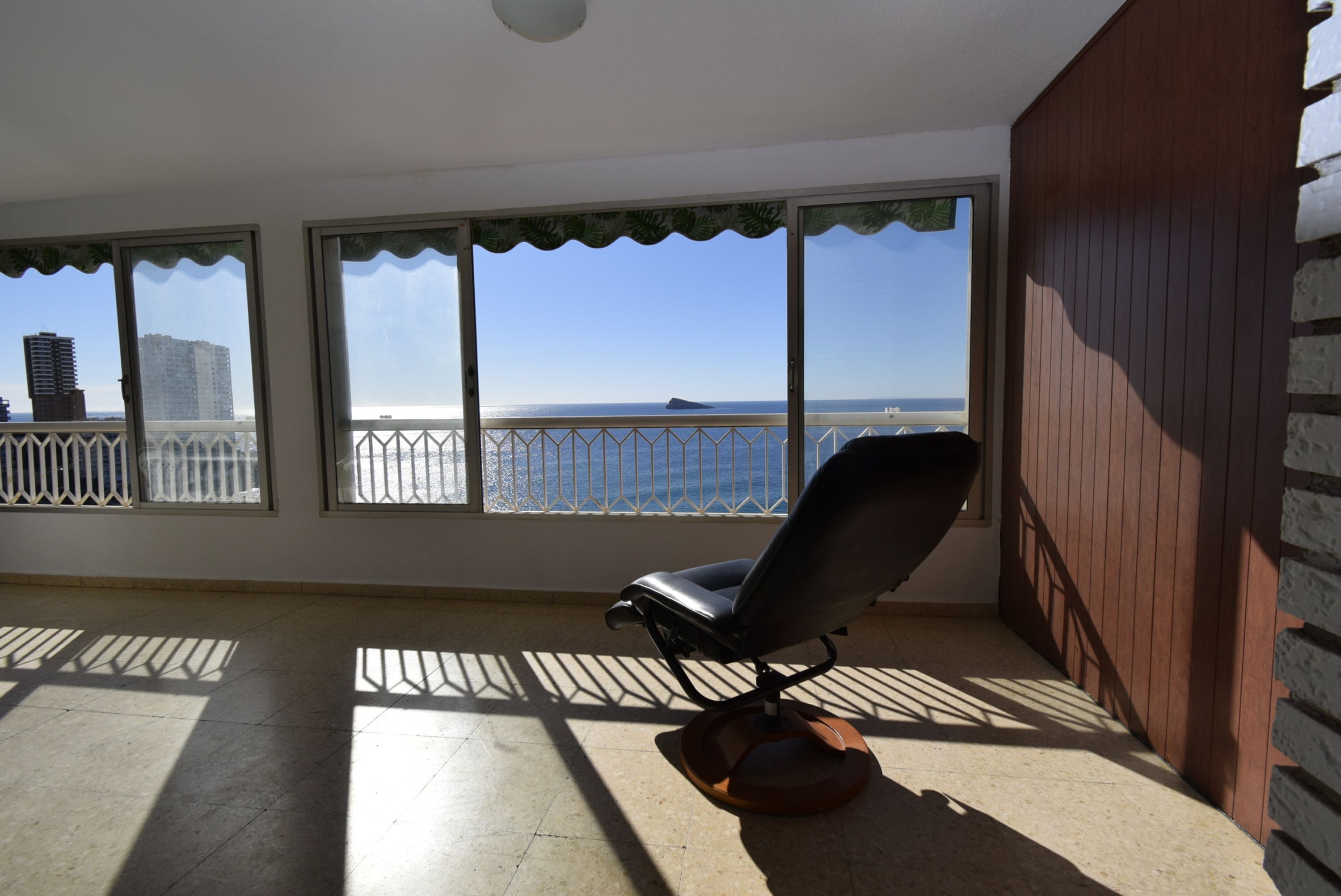 A balcony with a view of the sea, a chair, and a railing.