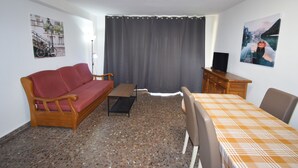 Quarto com sofá, mesa pequena, suporte para TV e cama com colcha xadrez.