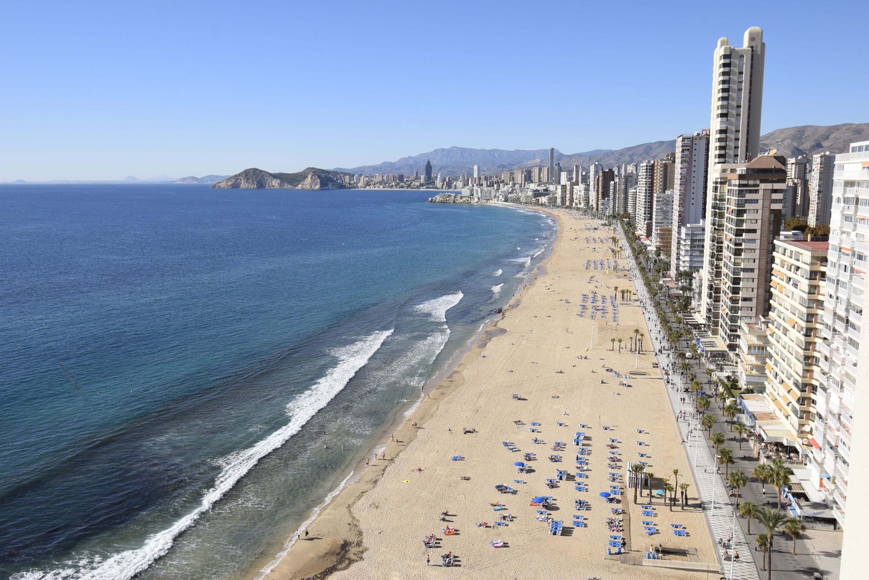 A coastal cityscape with a beach, high-rise buildings, and mountains in the background.