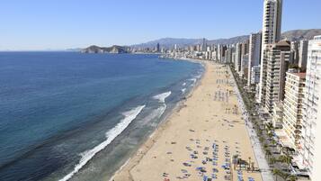 Un paisaje urbano costero con una playa, edificios altos y montañas al fondo.