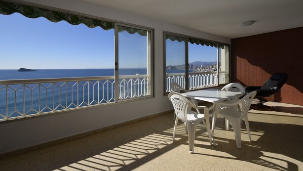 Varanda com vista para o mar, uma mesa com cadeiras e uma poltrona.