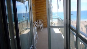 Un balcón con vistas a la playa, un muro de madera y una zona de estar con sillas de plástico.