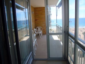 Ein Balkon mit Blick auf den Strand, eine Holzwand und eine Sitzecke mit Plastikstühlen.