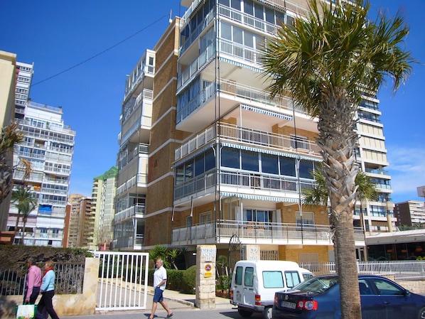 Ein mehrstöckiges Wohnhaus mit Balkonen, einem verschlossenen Eingang und einer Palme im Vordergrund.