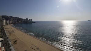 Una spiaggia con cielo sereno e sole, una riva sabbiosa e edifici lungo la costa.