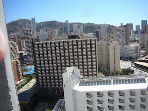 Ein Hochhaus mit mehreren Etagen, einer Dachterrasse und Blick auf eine Stadtlandschaft mit weiteren Gebäuden und einer Hügelkulisse im Hintergrund.