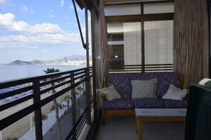Un balcón con vistas al mar, un sofá estampado y una ventana con cortinas.
