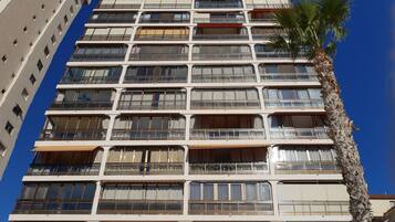 Un hotel de varios pisos con balcones, una palmera y un bar de aperitivos y restaurante a nivel de la calle.