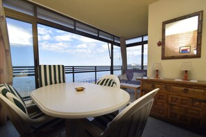 Ein Zimmer mit rundem Tisch, gestreifte Stühle, einer Couch, einem Holzschrank und einem großen Fenster mit Meerblick.
