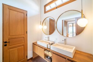 A bathroom with two sinks, wooden cabinetry, and a large mirror with round frames. - Villa Nusantara 6 in Pererenan (Pererenan)