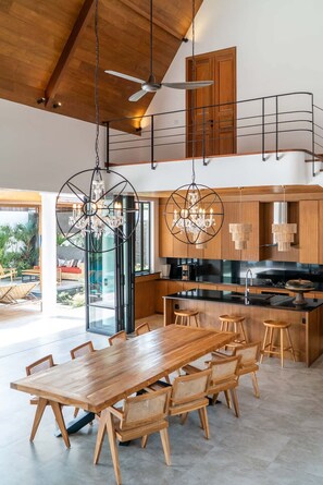 A modern kitchen with a wooden island, bar stools, and a dining table with chairs. - Villa Nusantara 6 in Pererenan (Pererenan)