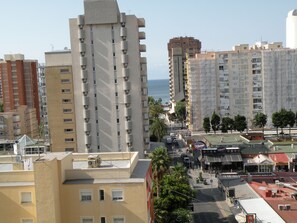 A cityscape with high-rise buildings, a street with parked cars, and a view of the sea. - Principado Centro 7 A (Benidorm)