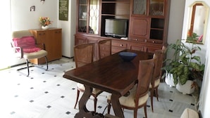 A dining area with a wooden table and chairs, a television on a cabinet, and a yellow hanging light fixture. - Principado Centro 7 A (Benidorm)