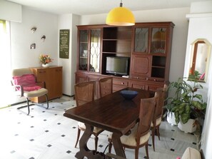 A dining area with a wooden table and chairs, a television on a cabinet, and a yellow hanging light fixture. - Principado Centro 7 A (Benidorm)
