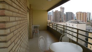 A balcony with a white table and chairs, a brick wall, and a view of tall buildings. - Principado Centro 7 A (Benidorm)