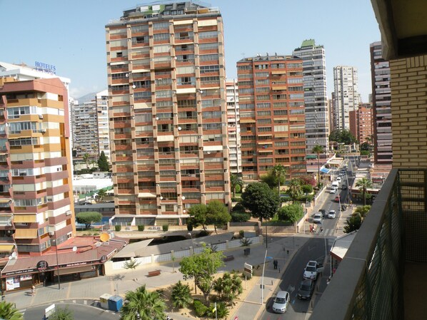 A high-rise building with multiple balconies, a street with cars, and a clear sky. - Principado Centro 7 A (Benidorm)