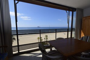 Ein Zimmer mit großem Fenster und Blick auf einen Strand, einem Holztisch und einem Stuhl.