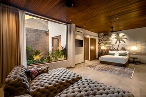 Ein modernes Schlafzimmer mit einem großen Bett, einer Couch und Blick auf einen Garten durch eine Schiebetür.