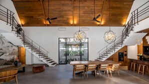 A spacious living area with a high ceiling, wooden staircase, and a dining table with chairs. - Villa Nusantara 3 in Pererenan (Pererenan)