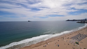 Una spiaggia con cielo sereno, mare calmo e una riva sabbiosa con ombrelloni e sedie.